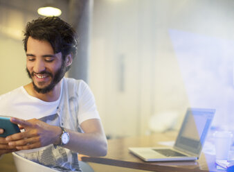 Lächelnder, lässiger Geschäftsmann, der mit seinem Handy im Büro SMS schreibt - CAIF13585