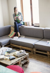 Creative businesswoman reading book at window in office - CAIF13594