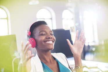 Smiling businesswoman listening to music on headphones in office with eyes closed - CAIF13606