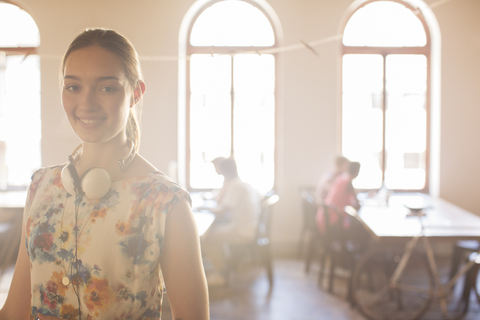 Porträt einer lächelnden Geschäftsfrau mit Kopfhörern in einem sonnigen Großraumbüro, lizenzfreies Stockfoto