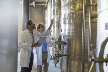 Vintners in lab coats checking vats in winery cellar - CAIF13623