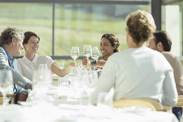 Freunde stoßen in einem sonnigen Restaurant mit Weingläsern an - CAIF13635