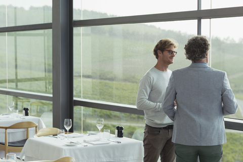 Männer unterhalten sich am Fenster des Speisesaals einer Weinkellerei, lizenzfreies Stockfoto