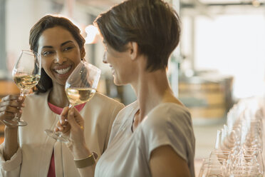 Smiling women wine tasting white wine in winery tasting room - CAIF13684