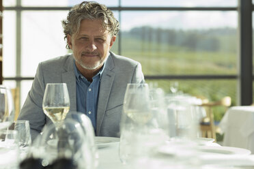 Porträt selbstbewusster Mann mit Weißwein am sonnigen Restauranttisch - CAIF13698