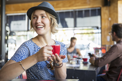 Lächelnde Frau trinkt Kaffee und schaut über die Schulter in einem Café, lizenzfreies Stockfoto