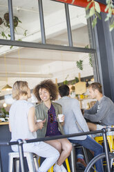 Friends drinking coffee and talking on urban cafe patio - CAIF13732