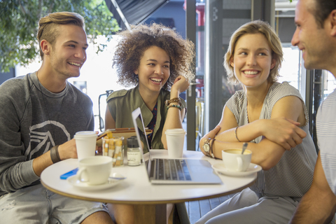 Freunde hängen mit Laptop und Kaffee auf der Terrasse eines Cafés ab, lizenzfreies Stockfoto