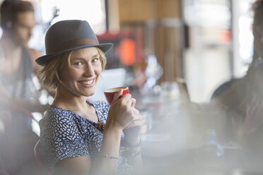 Porträt einer lächelnden Frau mit Hut, die in einem Café Espresso trinkt - CAIF13736