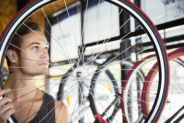 Junger Mann untersucht die Speichen eines Rades in einem Fahrradgeschäft - CAIF13743