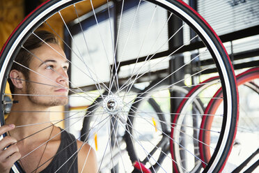 Young man examining spokes on wheel in bicycle shop - CAIF13743