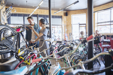 Couple browsing bicycles on rack in bicycle shop - CAIF13747