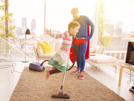 Superhelden-Vater staubsaugt, während Tochter im Wohnzimmer springt - CAIF13757