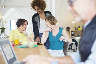 Smiling office workers talking at desk during break - CAIF13776