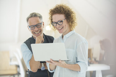 Two smiling office workers using laptop - CAIF13780