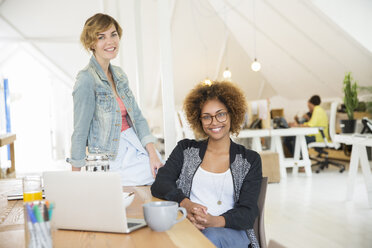 Portrait of women smiling in office with laptop on desk - CAIF13805