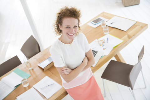 Porträt einer Frau mit verschränkten Armen, lächelnd im Büro, lizenzfreies Stockfoto