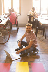 Porträt eines kreativen Geschäftsmannes, der am Laptop auf dem Boden arbeitet - CAIF13836