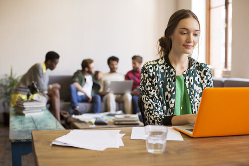 Kreative Geschäftsfrau bei der Arbeit am Laptop mit Papierkram im Büro - CAIF13846