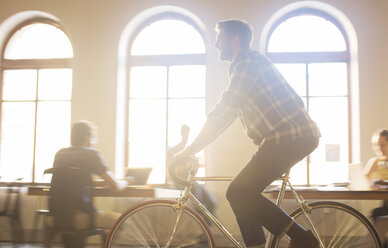 Lässiger Geschäftsmann fährt Fahrrad im sonnigen Büro - CAIF13856