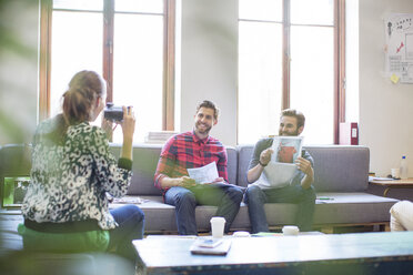 Kreativer Geschäftsmann posiert mit Foto für Mitarbeiter mit Sofortbildkamera im Büro - CAIF13874