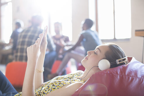 Lässige Geschäftsfrau entspannt sich mit Kopfhörern und digitalem Tablet auf einem Sitzsack - CAIF13902