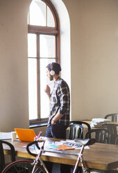 Pensive creative businessman with headphones looking out office window - CAIF13904