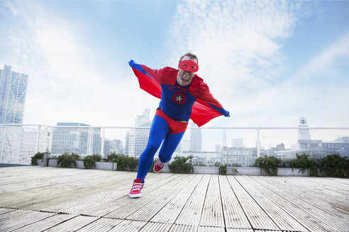 Superheld läuft mit Umhang auf dem Dach der Stadt - CAIF13931