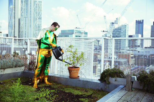 Superheld bewässert Topfpflanze auf dem Dach der Stadt - CAIF13936