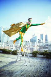 Superhero posing on stepladder on city rooftop - CAIF13937