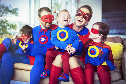 Superheldenfamilie lachend auf dem Sofa - CAIF13938