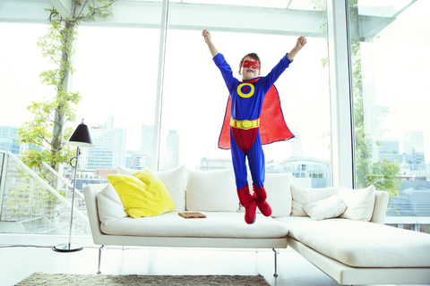 Junge Superheld springt vom Wohnzimmersofa, lizenzfreies Stockfoto