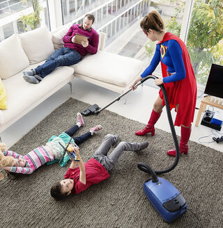 Superheld beim Staubsaugen um die Familie herum im Wohnzimmer - CAIF13944
