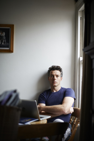 Man sitting at table with open laptop looking away stock photo