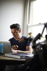 Mann arbeitet zu Hause am Laptop und isst einen Apfel - CAIF13982