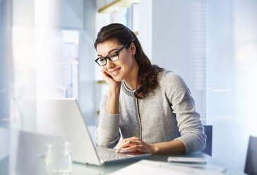 Weibliche Büroangestellte sitzt am Schreibtisch und benutzt einen Laptop - CAIF13997
