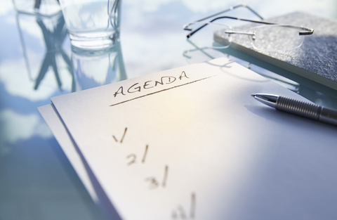 Close up of desk with,glass,glasses and note saying 'agenda',pen stock photo