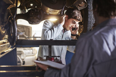 Mechaniker und Kunde telefonieren unter dem Auto - CAIF14066