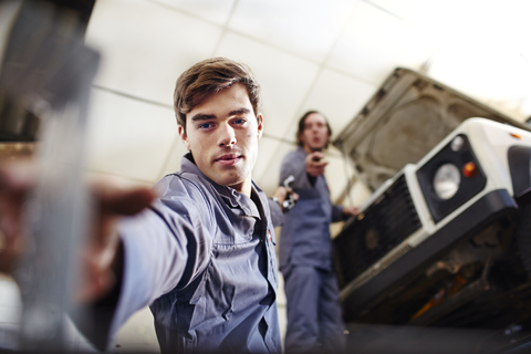 Mechaniker greift in einer Autowerkstatt nach einem Werkzeug unter dem Auto, lizenzfreies Stockfoto