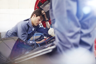 Frustrierter Mechaniker schaut in einer Autowerkstatt auf den Motor hinunter - CAIF14072