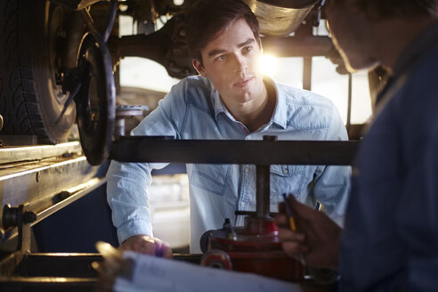 Mechaniker und Kunde im Gespräch unter dem Auto in der Autowerkstatt - CAIF14073