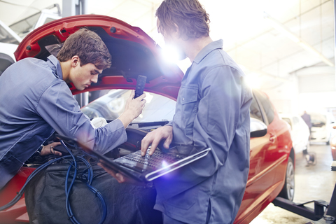 Mechanics with laptop working on car engine in auto repair shop stock photo