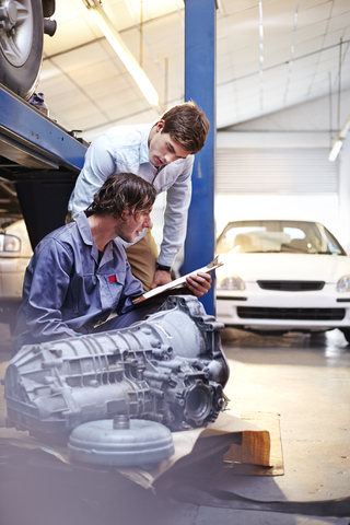 Mechaniker mit Klemmbrett im Gespräch mit einem Kunden in einer Autowerkstatt, lizenzfreies Stockfoto