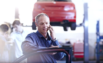 Mann spricht mit Handy in Autowerkstatt - CAIF14084