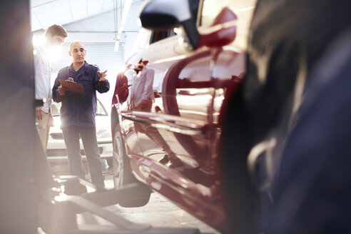 Mechaniker mit Klemmbrett im Gespräch mit einem Kunden in einer Autowerkstatt - CAIF14093