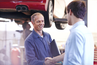 Mechanic and customer handshaking in auto repair shop - CAIF14094