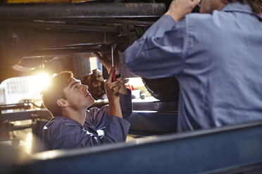 Mechanics working under car in auto repair shop - CAIF14096