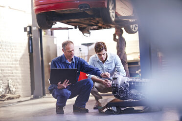 Mechanic and customer with laptop examining engine in auto repair shop - CAIF14097