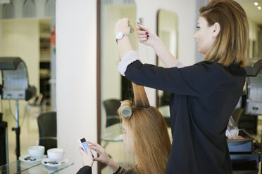 Friseurin wickelt das Haar einer Kundin in Lockenwickler im Salon - CAIF14100