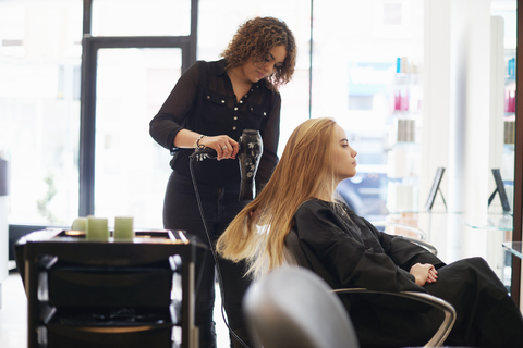 Friseurin trocknet langes Haar einer Kundin im Salon, lizenzfreies Stockfoto
